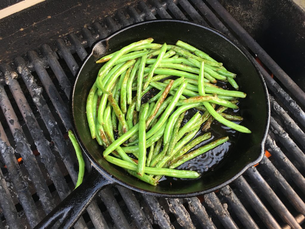 cast iron skillet with green beans on a hot grill 