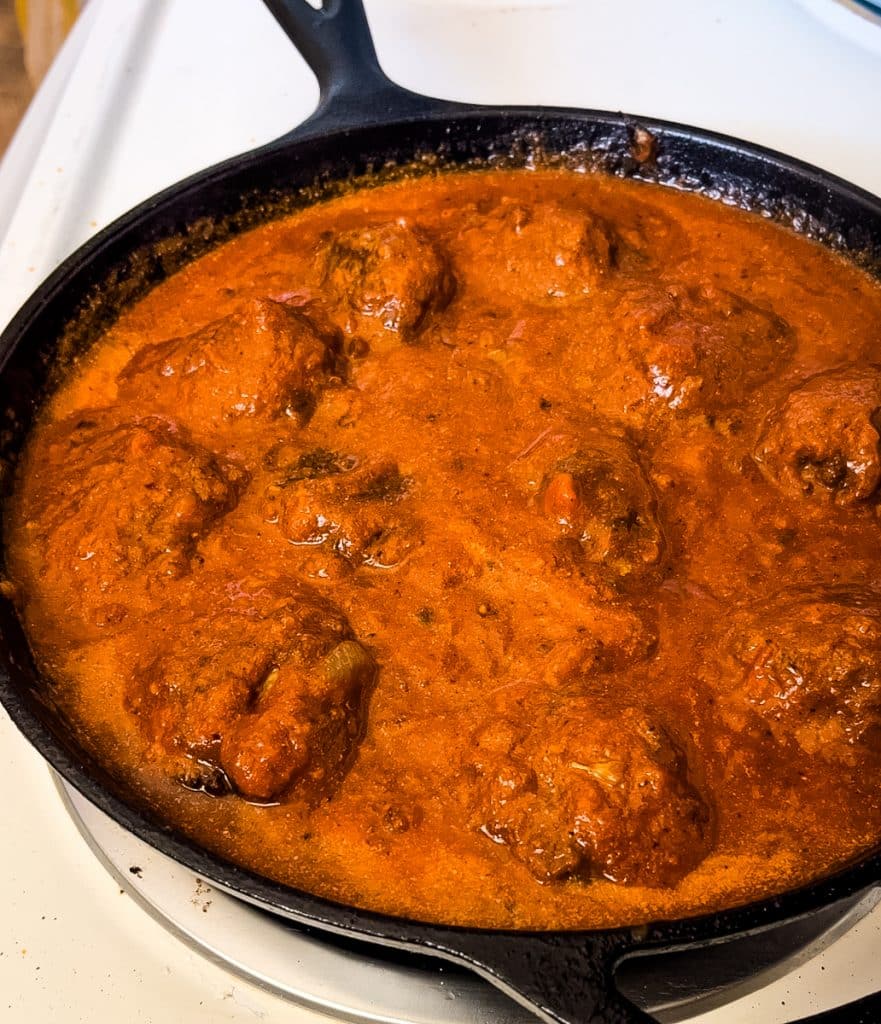 meatballs simmering in red sauce on the stove