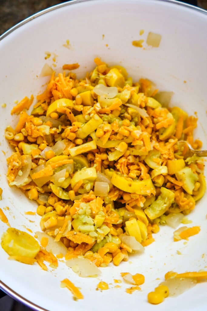 Bowl of steamed squash, onions, corn, and sharp cheddar cheese ready for baking.