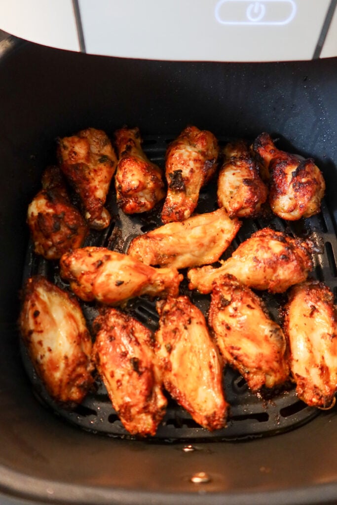 Golden brown chicken wings cooking inside an air fryer basket.
