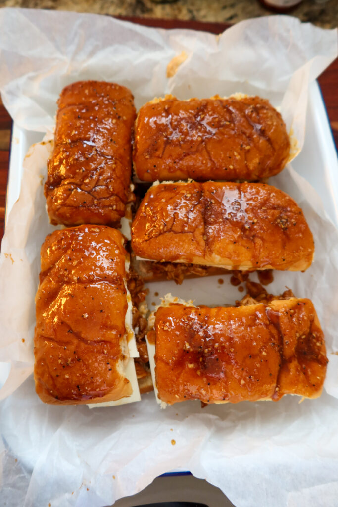 Unbaked BBQ chicken sliders in a parchment-lined baking dish, topped with honey-butter glaze.
