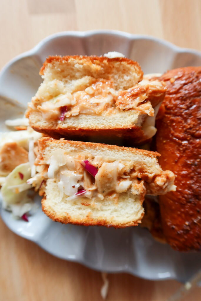 Close-up of BBQ chicken sub slider sliced in half, filled with BBQ chicken, cheese, and coleslaw on a plate.