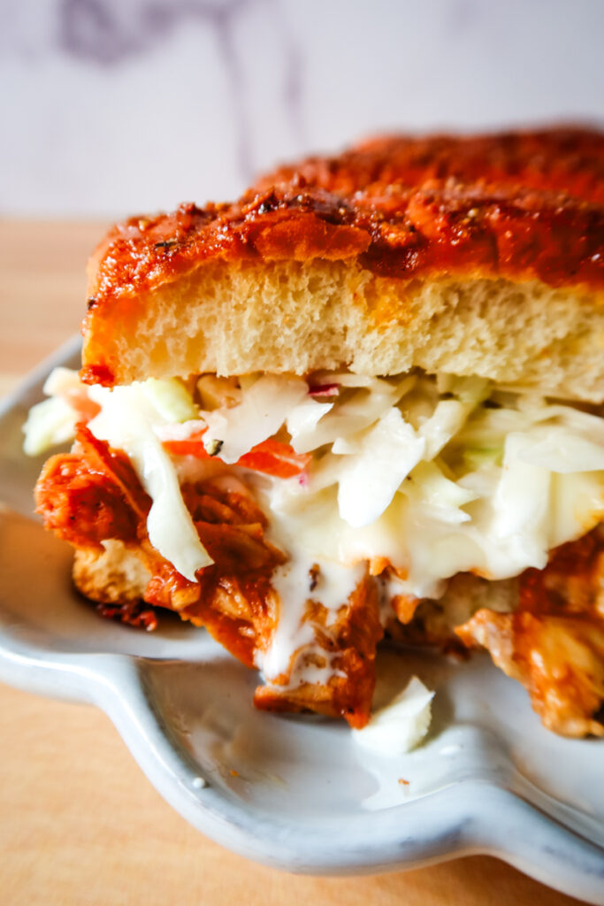 BBQ chicken sub slider with melted cheese and fresh coleslaw inside a glazed Hawaiian roll.