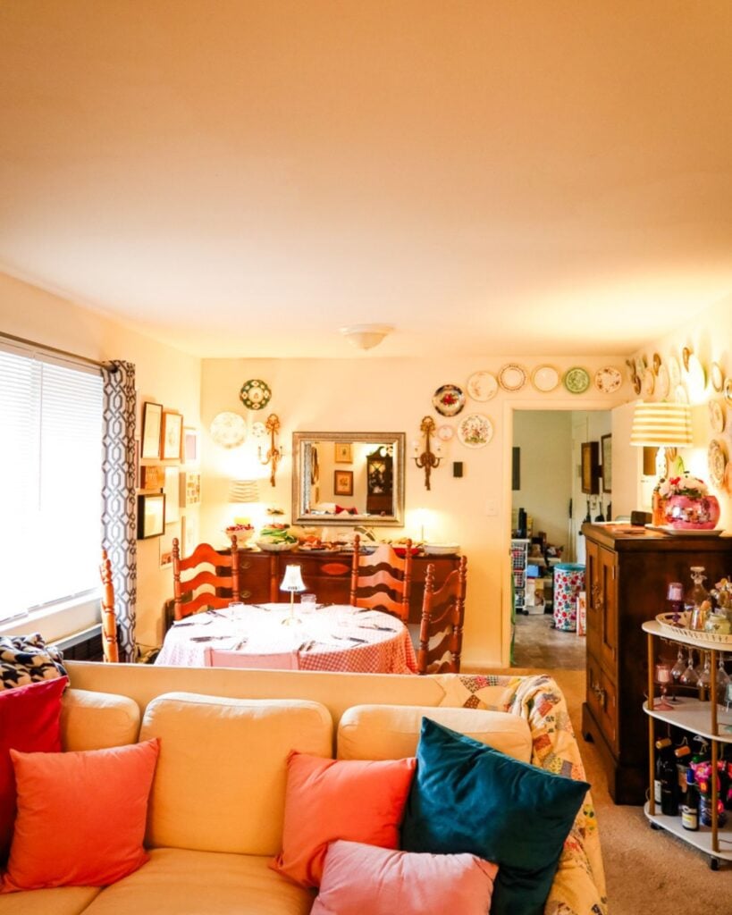 Warmly lit living room with a sofa of colorful pillows and a buffet table set with appetizers.