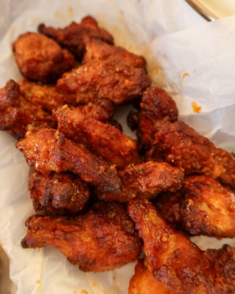 Tray of crispy lemon pepper hot wings with golden charred edges on parchment paper.