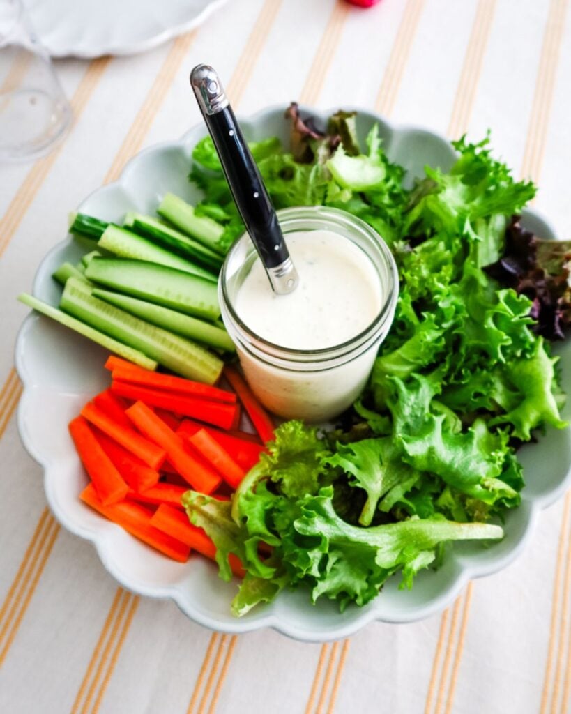 Platter of fresh lettuce, carrots, cucumbers, and dip in a mason jar at the center.