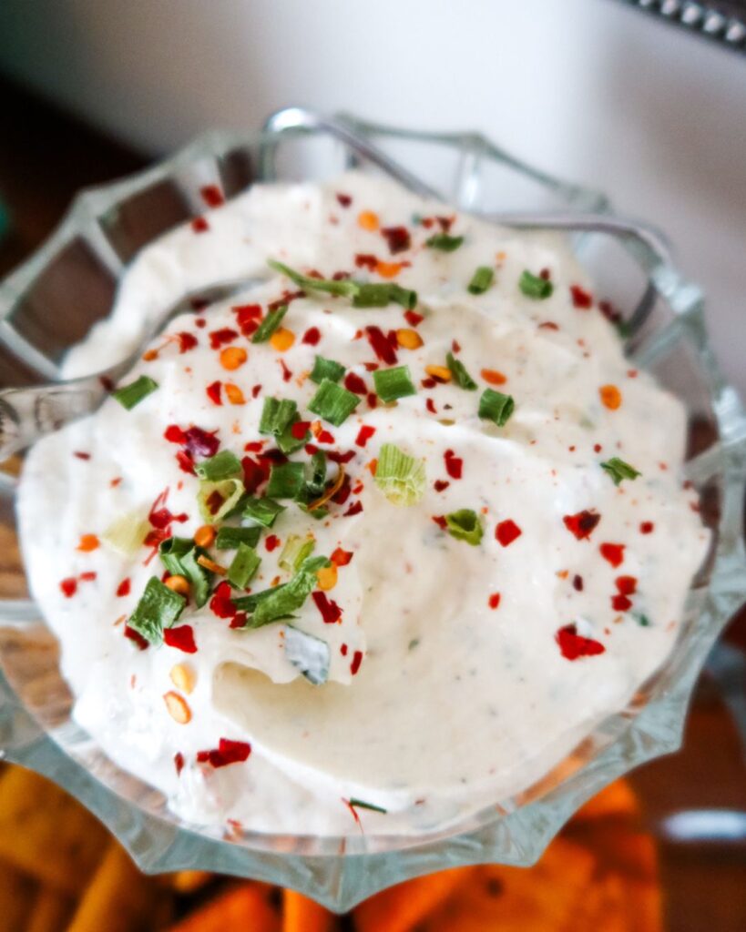 Bowl of creamy Firecracker Dip with fiery seasoning, surrounded by veggie sticks and chips.