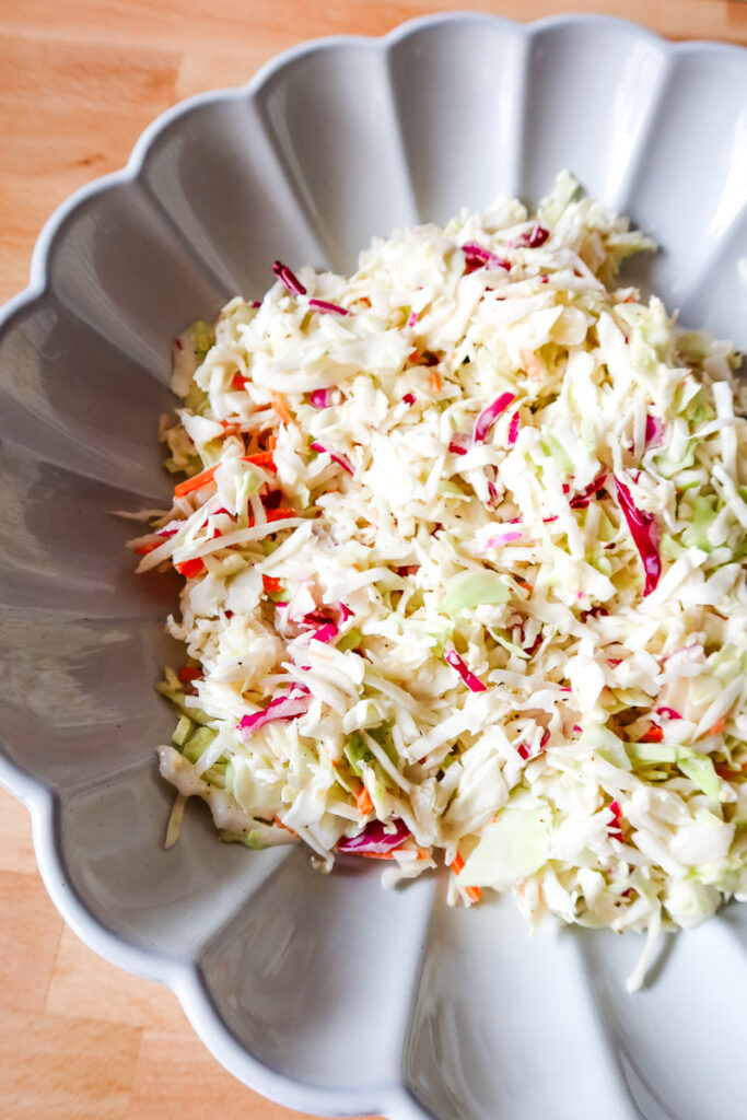 Overhead photo of creamy homemade coleslaw in a scalloped white bowl with a spoon.