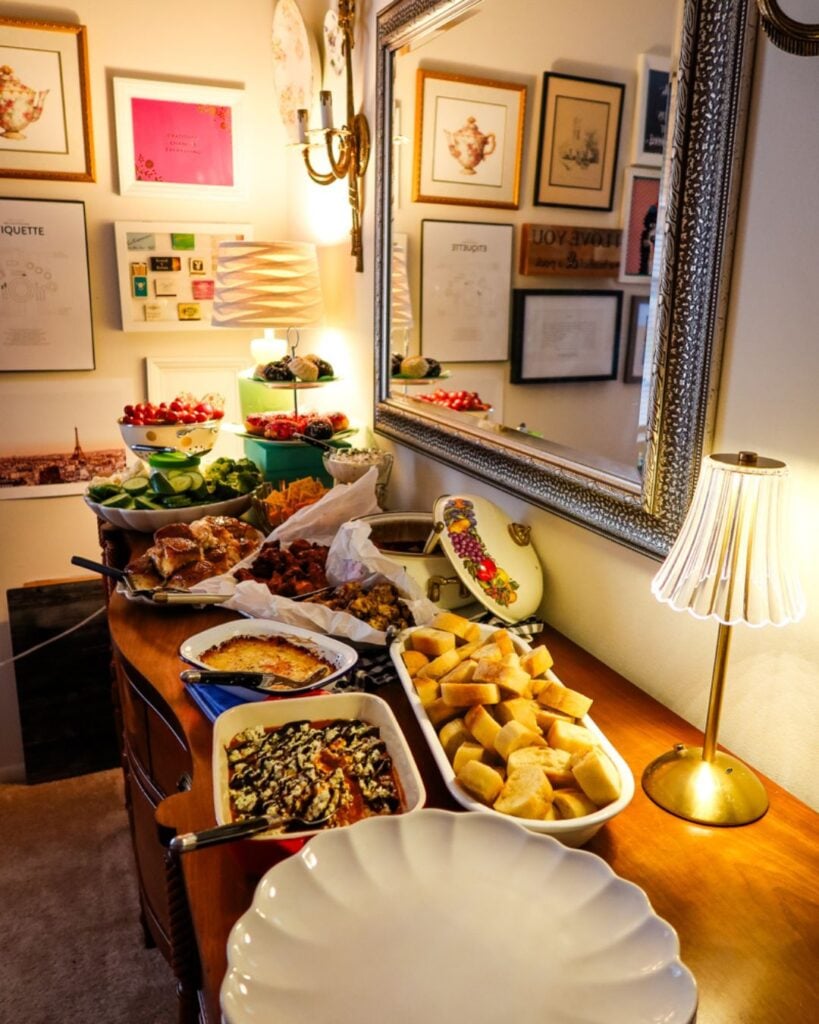 uffet table featuring appetizers, dips, breads, and desserts set under a warm lamp.