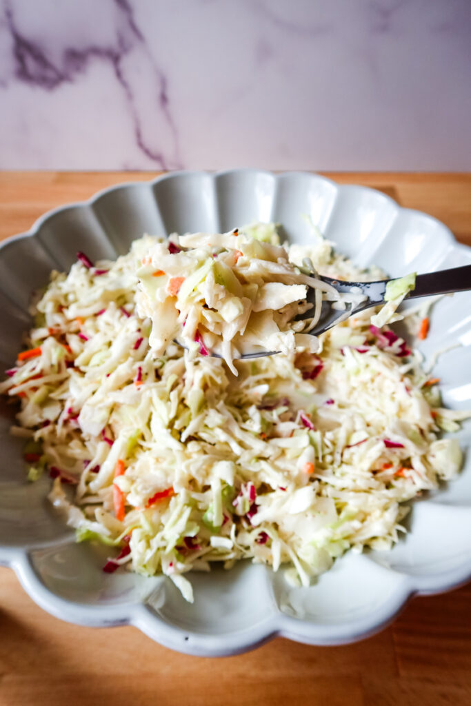 A spoonful of creamy coleslaw being lifted from a scalloped bowl full of fresh slaw.