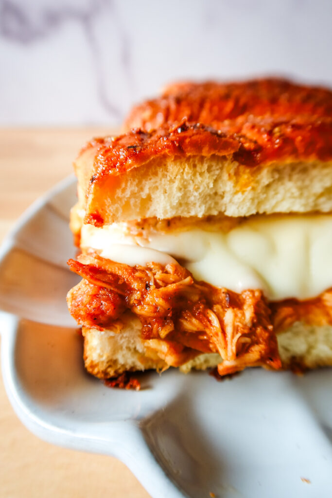 Close-up of BBQ chicken and melted cheese inside Hawaiian slider roll.