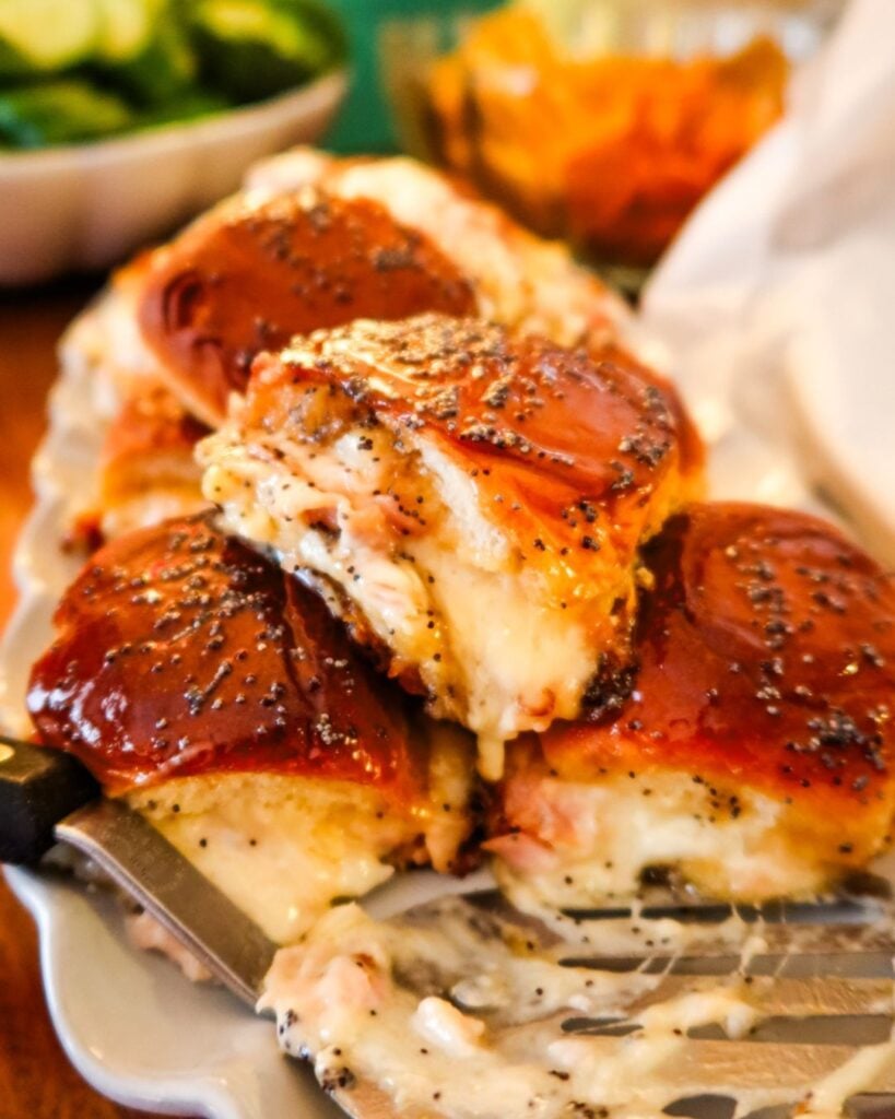 Golden baked ham and cheese sliders topped with poppy seeds and oozing with melted cheese.