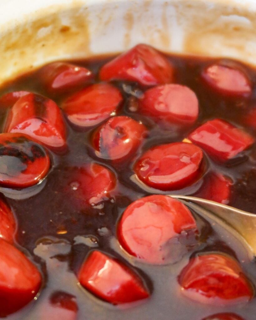 Close-up of sliced kielbasa in a glossy teriyaki glaze with a serving spoon.