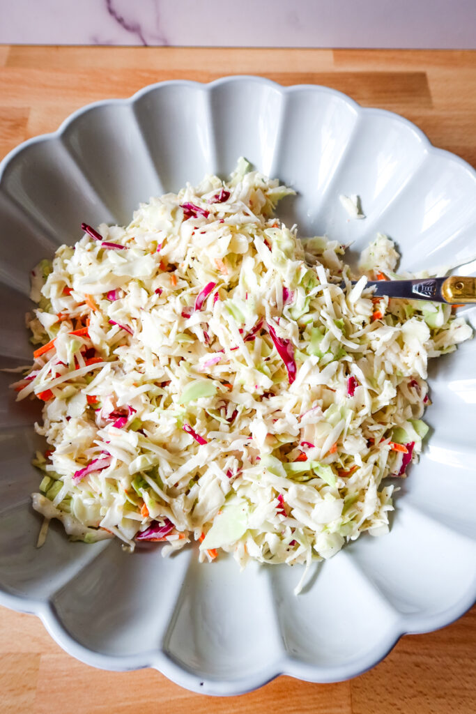Top-down shot of coleslaw in a scalloped serving dish with flecks of purple and green cabbage.