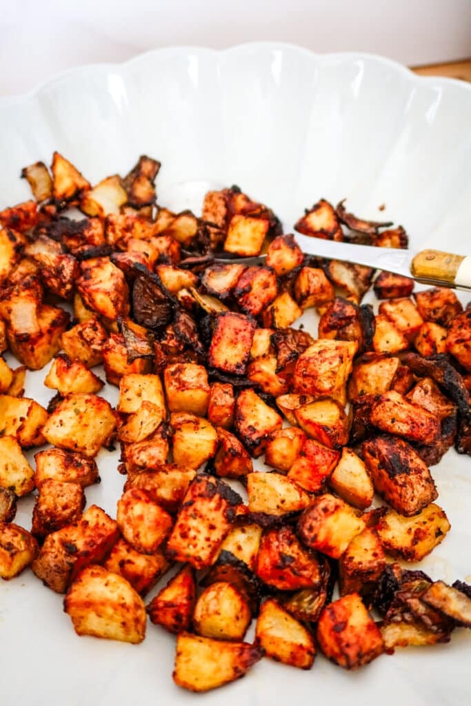 Air fryer roasted potatoes and onions with charred edges and vibrant orange-red seasoning on a white plate.