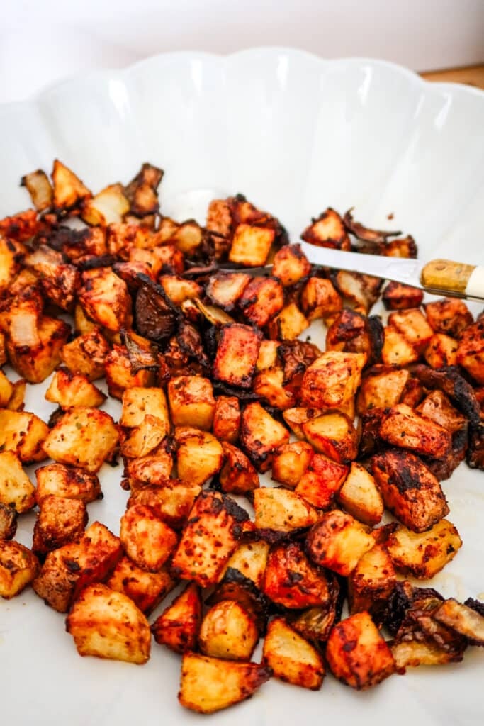 Close view of air-fried potato cubes and onions tossed in spicy red Firecracker seasoning on a white serving plate.
