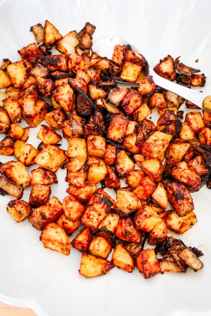 Overhead shot of crispy air-fried potato cubes and onion chunks seasoned with Firecracker spice blend in a scalloped dish.