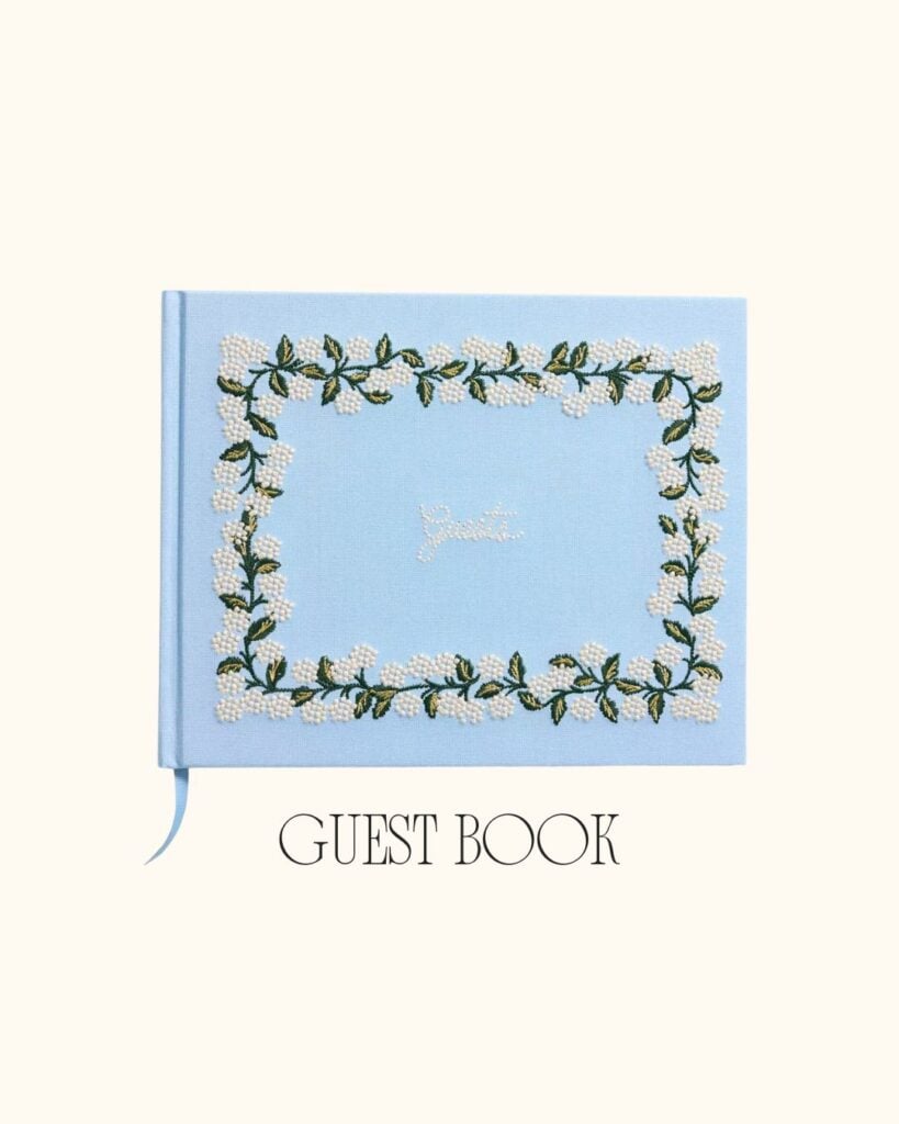 Light blue embroidered guest book with floral and pearl details, styled flat on a neutral background.