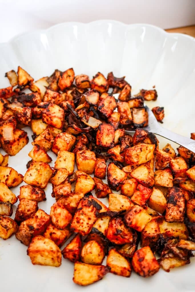 Close-up of crispy diced potatoes and onions with a spicy red seasoning, air fried to golden perfection in a scalloped serving bowl.