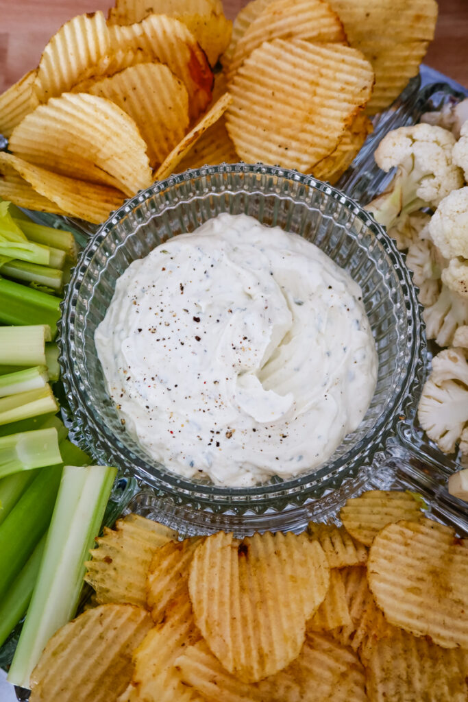Overhead shot of a snack platter with a bowl of creamy ranch dip surrounded by chips, celery, and cauliflower.
