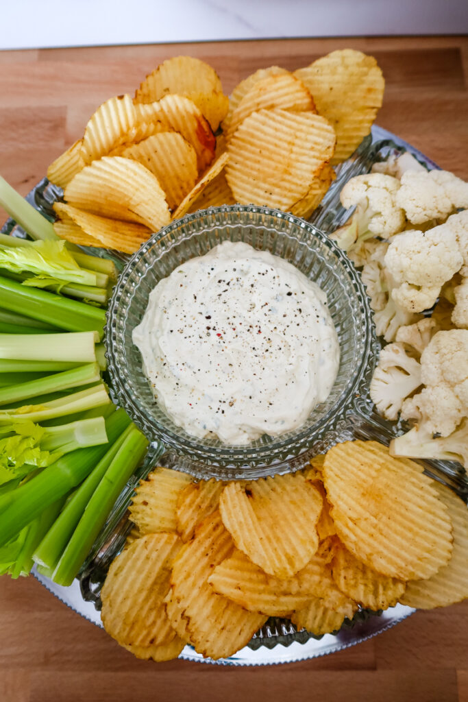 Overhead view of a serving tray filled with homemade ranch dip, celery, cauliflower, and potato chips.