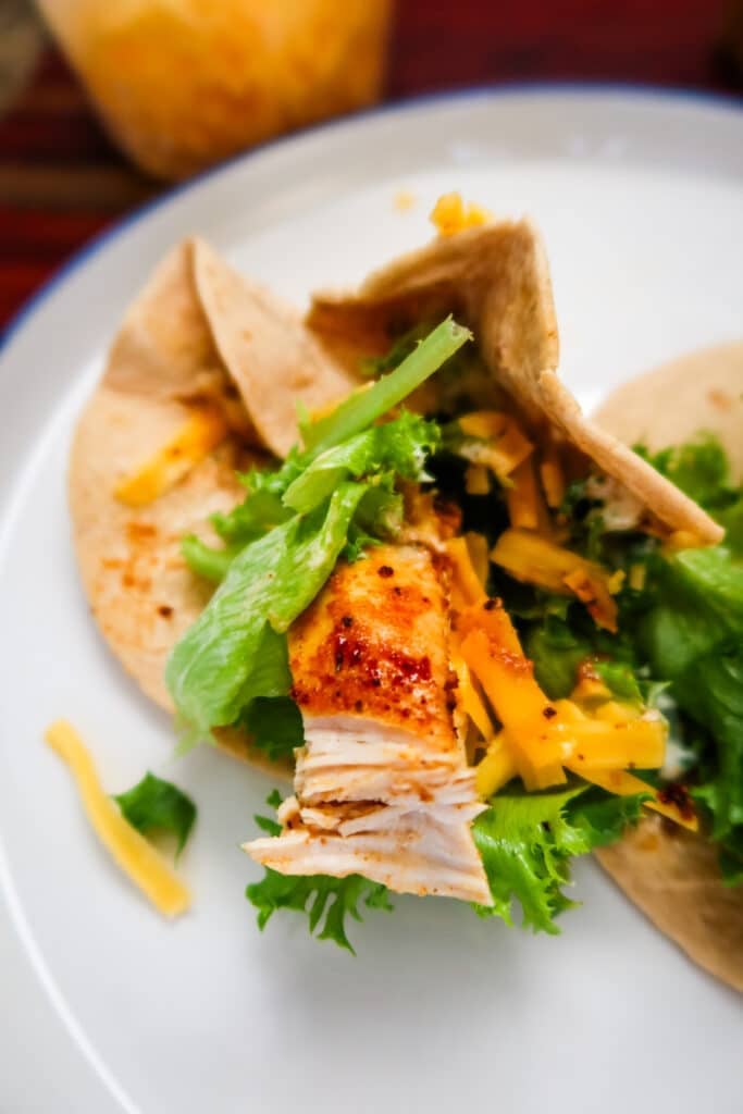 Air fryer chicken wraps on a plate with shredded cheddar and dressing jar in the background.