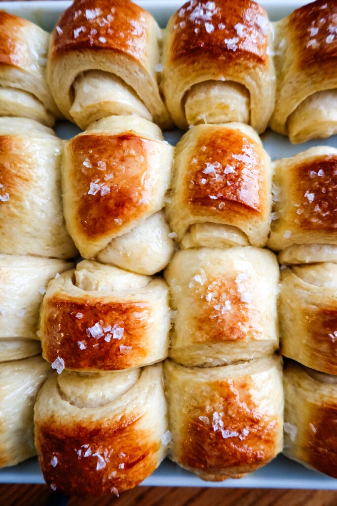 Close-up of golden-brown Parkerhouse rolls topped with flaky sea salt.