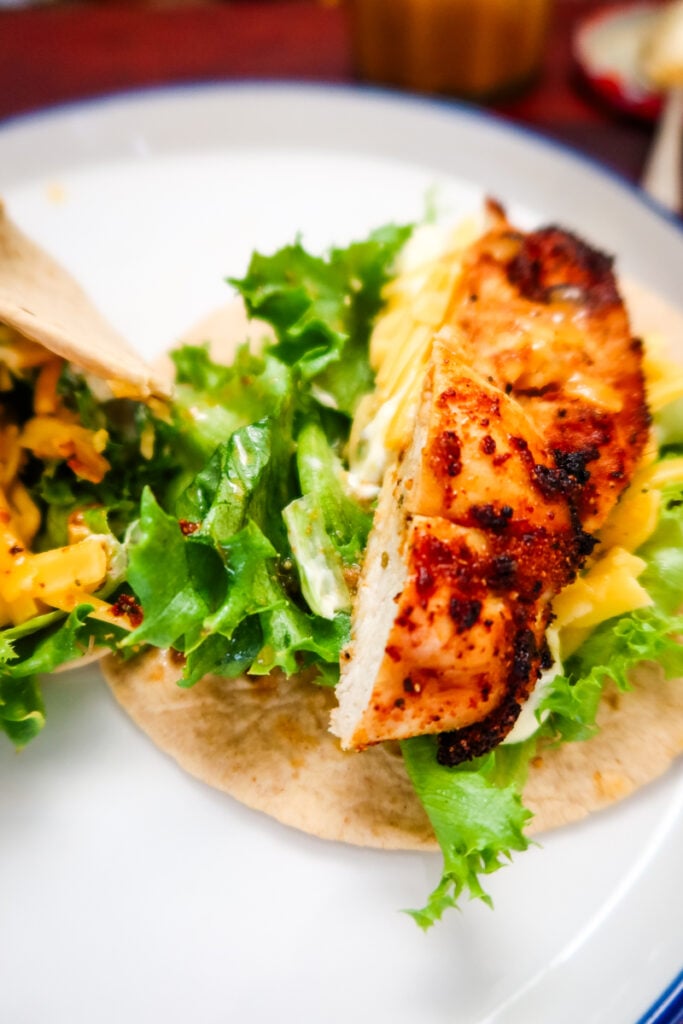 Close-up of sliced air fryer chicken with lettuce and cheddar inside a tortilla wrap.