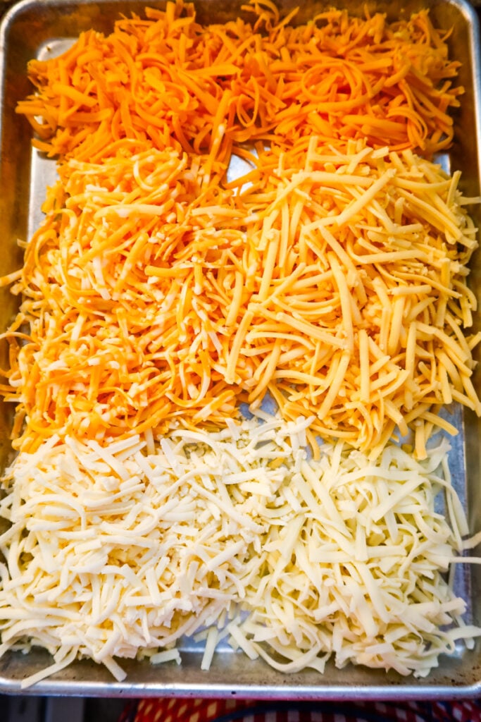 A sheet pan filled with piles of freshly hand-grated cheddar, gouda, colby jack, muenster, and mozzarella cheese for macaroni and cheese.
