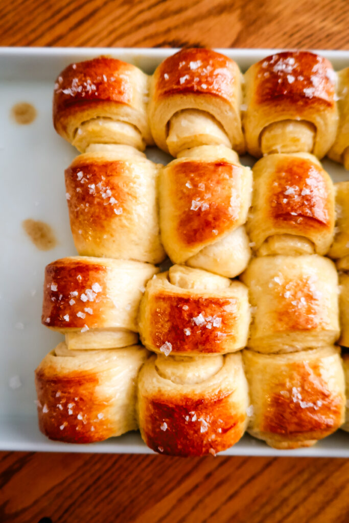 Side view of golden Parkerhouse rolls baked together in a white baking dish.