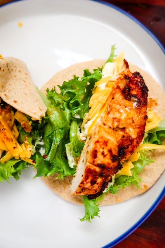 Two open chicken snack wraps with lettuce, cheese, and sliced air fryer chicken on a plate.