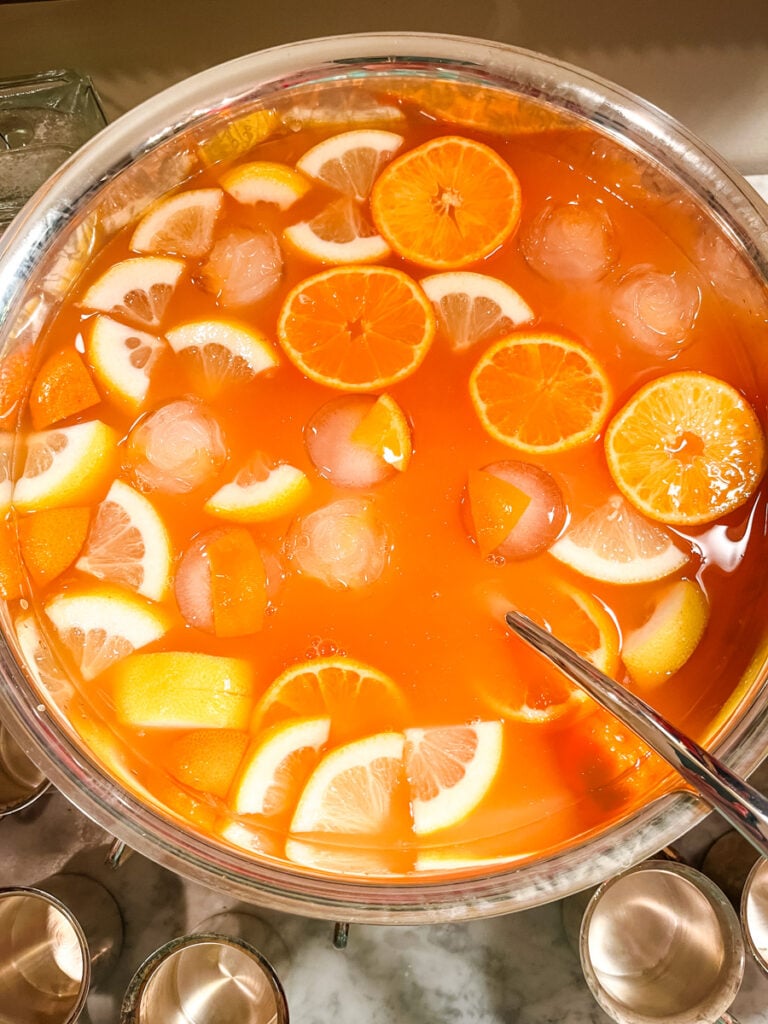 Jingle Juice Christmas punch with orange and lemon slices floating in a silver punch bowl on a holiday bar