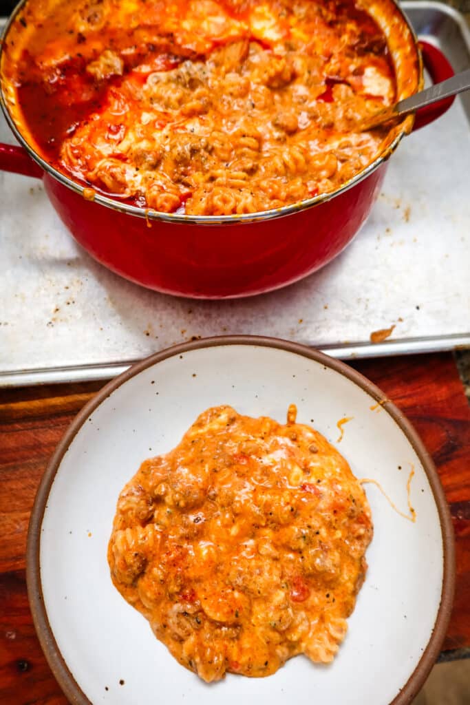 A pot of baked lasagna soup with a bowl served in front on a wooden board.