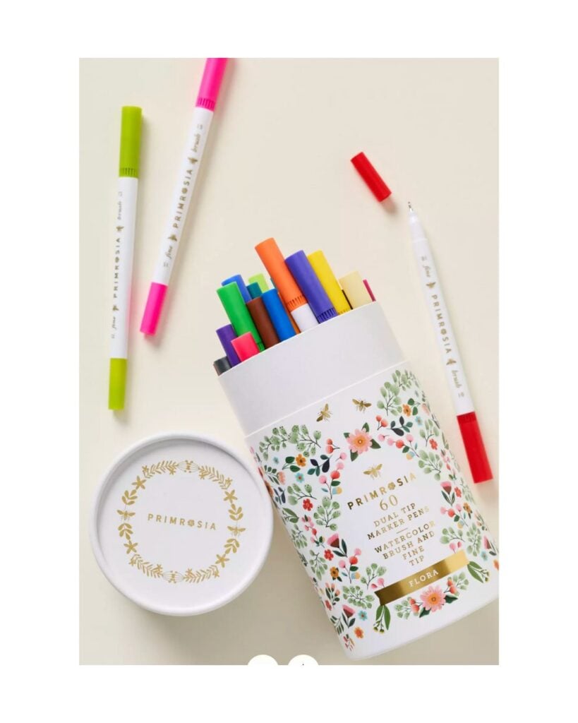 Floral tin of dual-tip markers with colorful pens scattered nearby