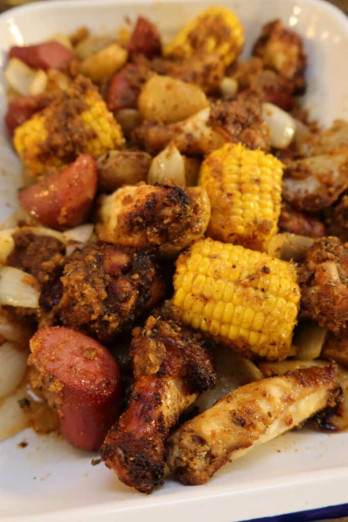 Air fryer chicken wing boil served in a white baking dish with sausage, corn, onions, and seasoned potatoes.