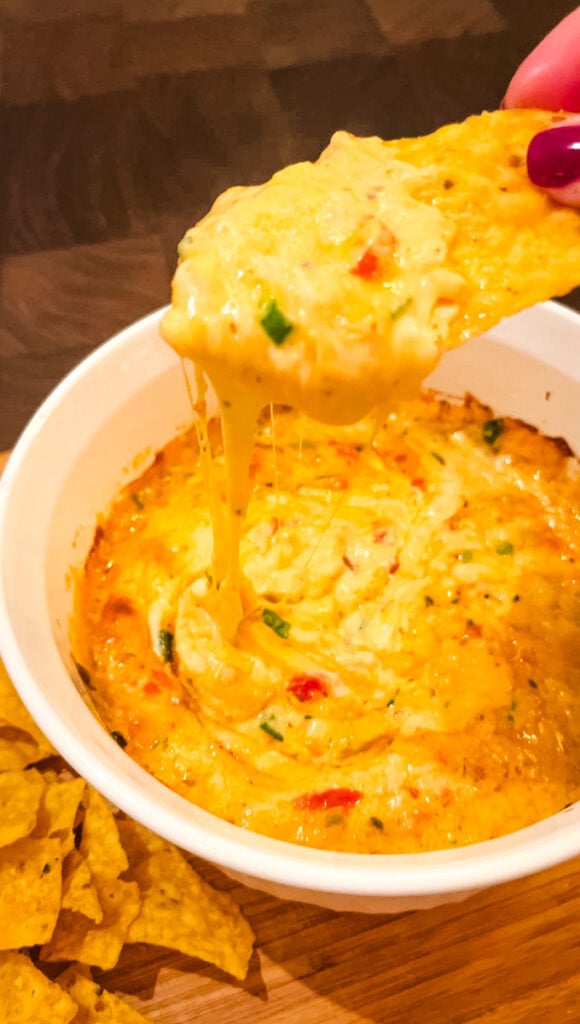 hand dipping tortilla chip into hot baked pimento cheese dip with melted cheese pull