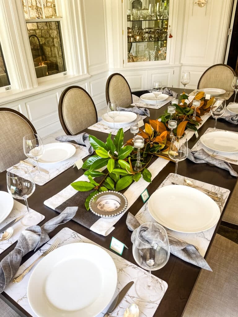 Elegant dinner party table set with plates, napkins, wine glasses, and greenery centerpiece