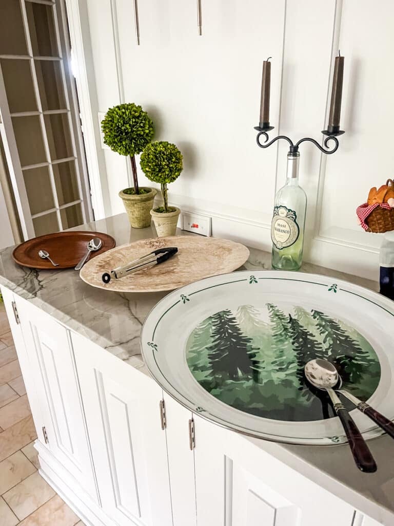 Dinner party serving station with empty platters, serving utensils, and decor on countertop