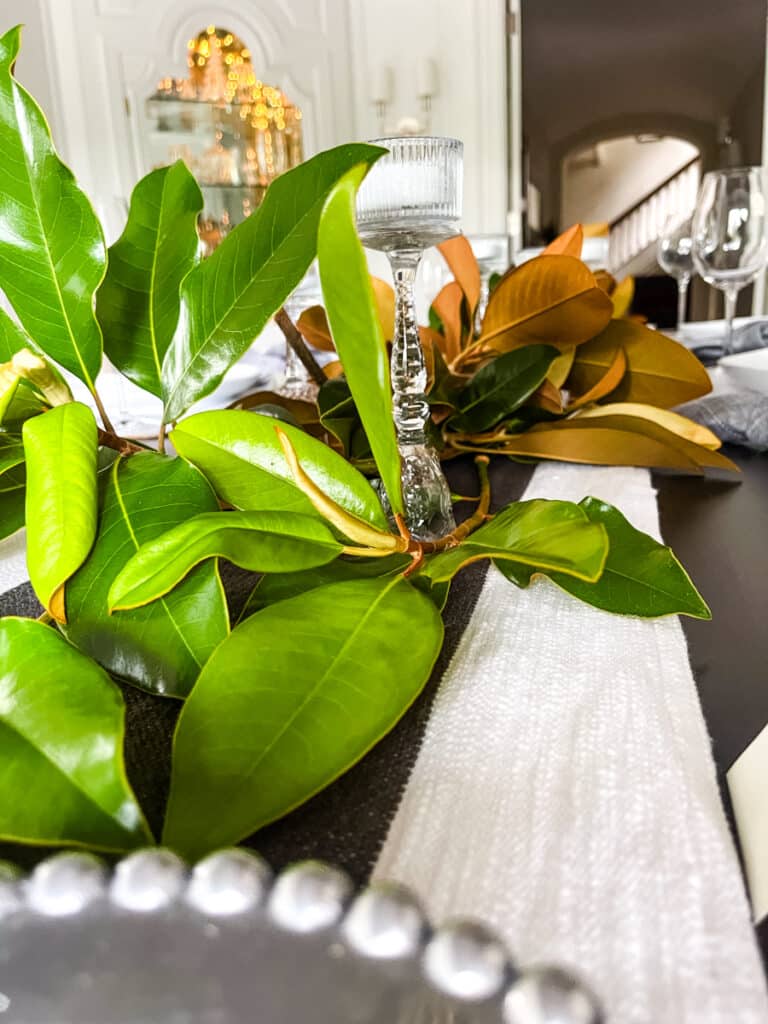 Elegant dinner party table with greenery runner, glass candle holders, and neutral place settings