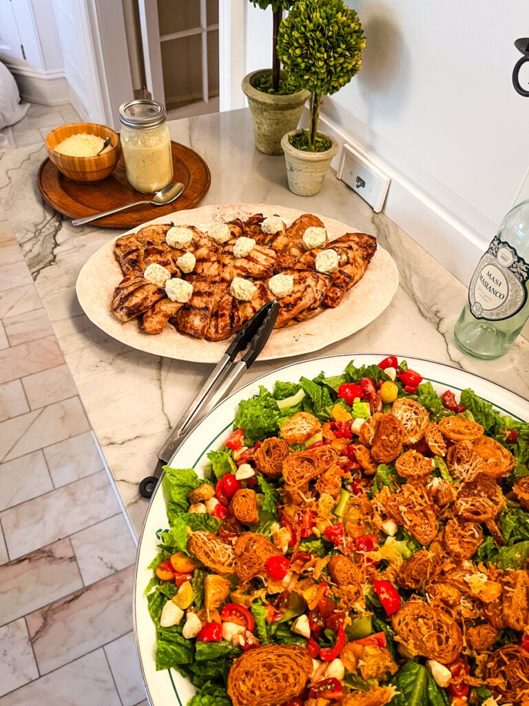 Dinner party spread with grilled steakhouse chicken and caprese caesar salad on marble counter