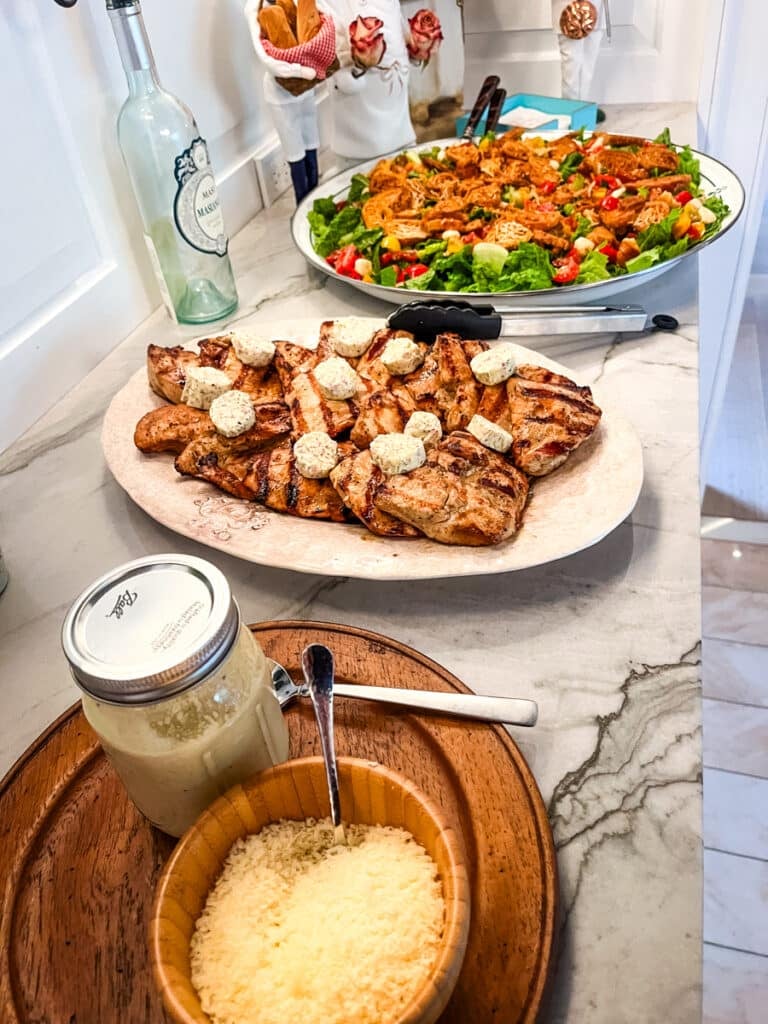 Dinner party food spread with grilled chicken and caprese caesar salad on marble counter