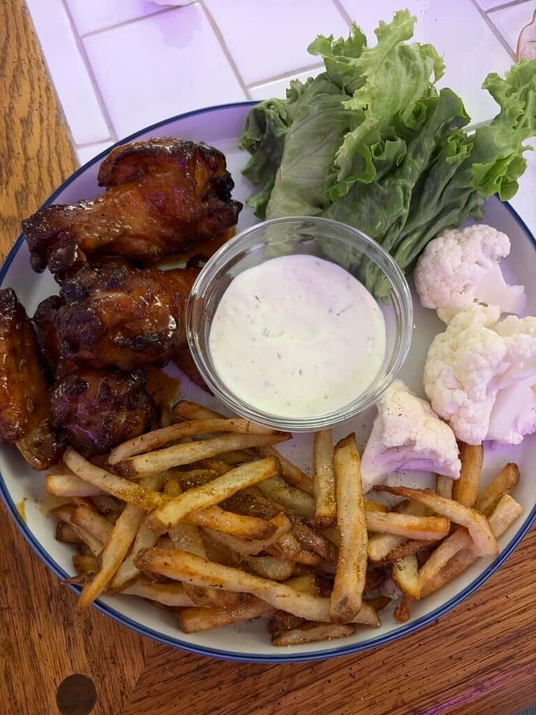 Glazed chicken wings served with crispy French fries, green lettuce, cauliflower florets, and a bowl of creamy ranch dressing.