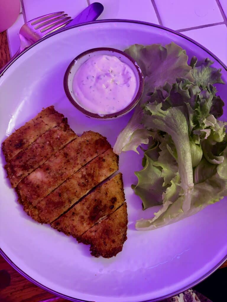 Crispy sliced chicken cutlet served with green leaf lettuce and a small bowl of creamy homemade ranch dressing on a white plate.