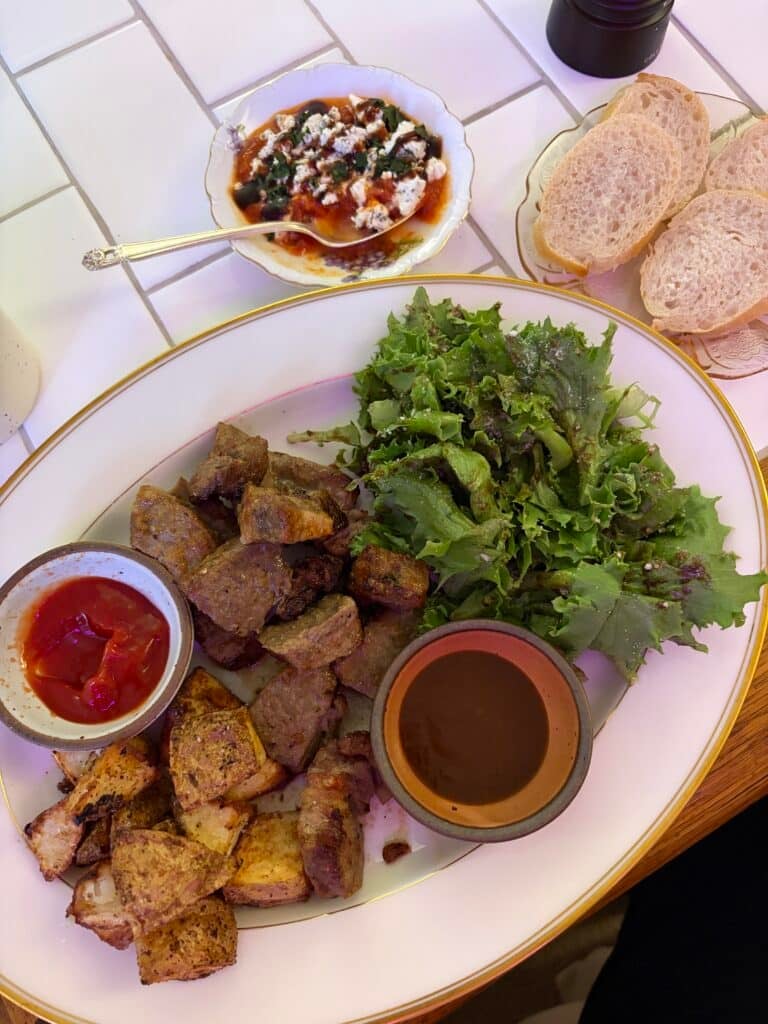 Sliced steak, crispy roasted potatoes, green lettuce, ketchup, and steak sauce served together on a large white platter.