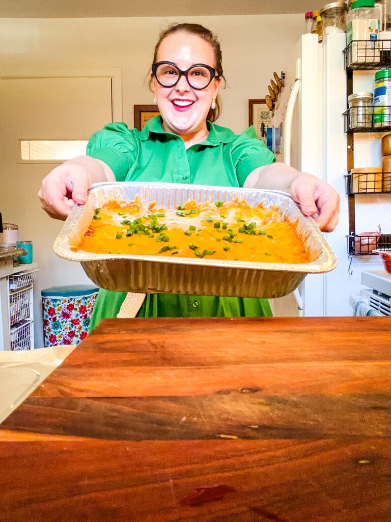 Woman holding a large baking pan of cheesy pulled pork enchiladas prepared as part of a two-pan family dinner recipe.