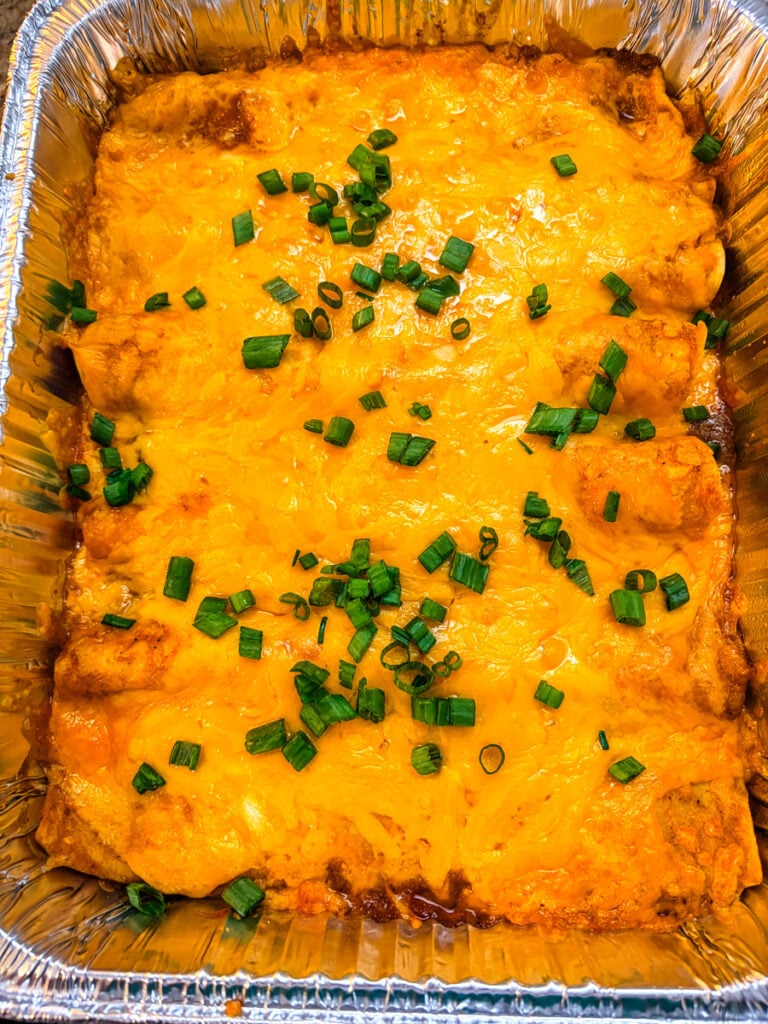 Finished pan of pulled pork enchiladas topped with melted cheddar cheese and red sauce; the recipe also includes a rotisserie chicken variation.