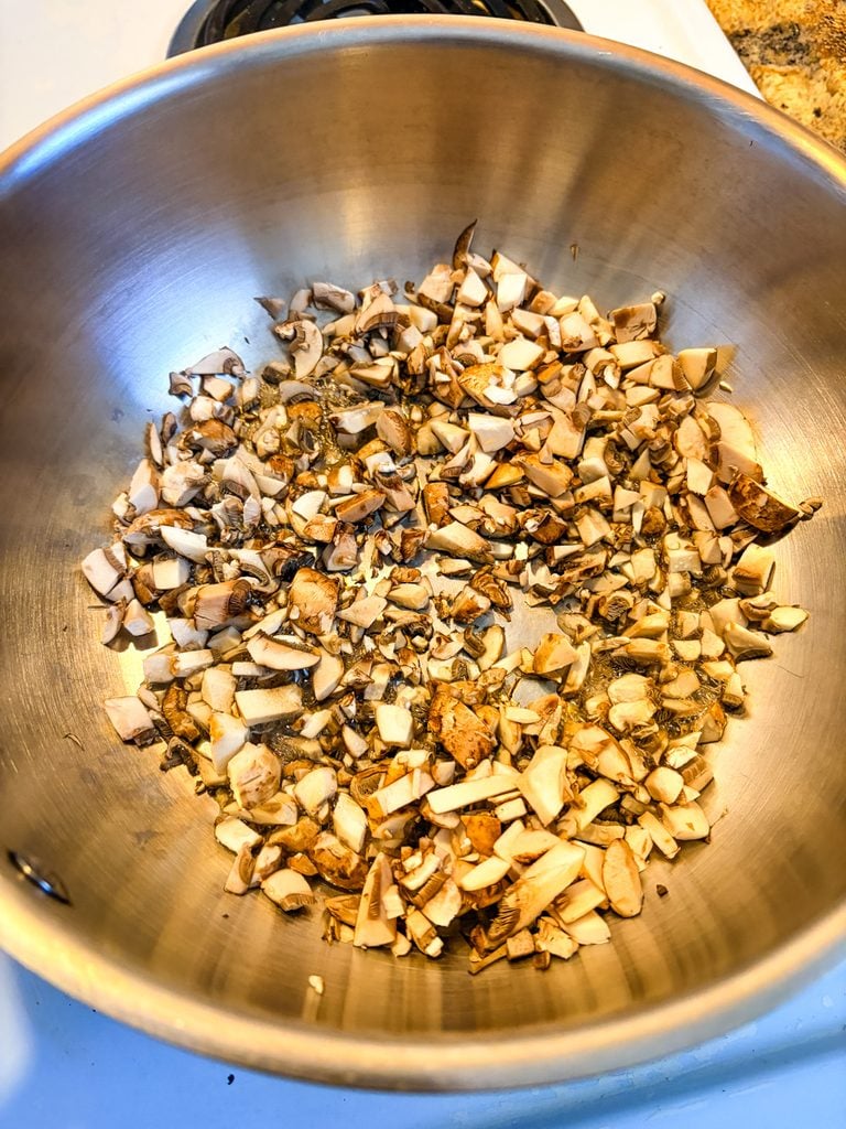 Finely chopped button mushrooms cooking in a dry stainless steel saucier pan before adding butter