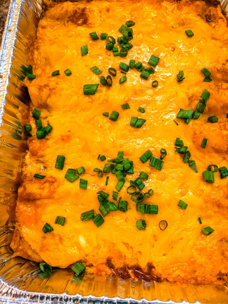 wo aluminum baking pans filled with cheesy pulled pork enchiladas, showing a big-batch dinner that can be prepared ahead.