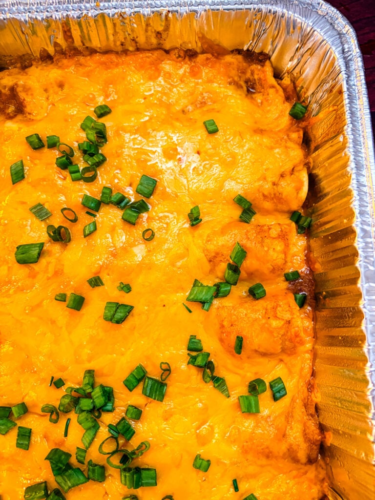Close-up of baked pulled pork enchiladas with golden melted cheddar cheese and red sauce in a foil baking dish.